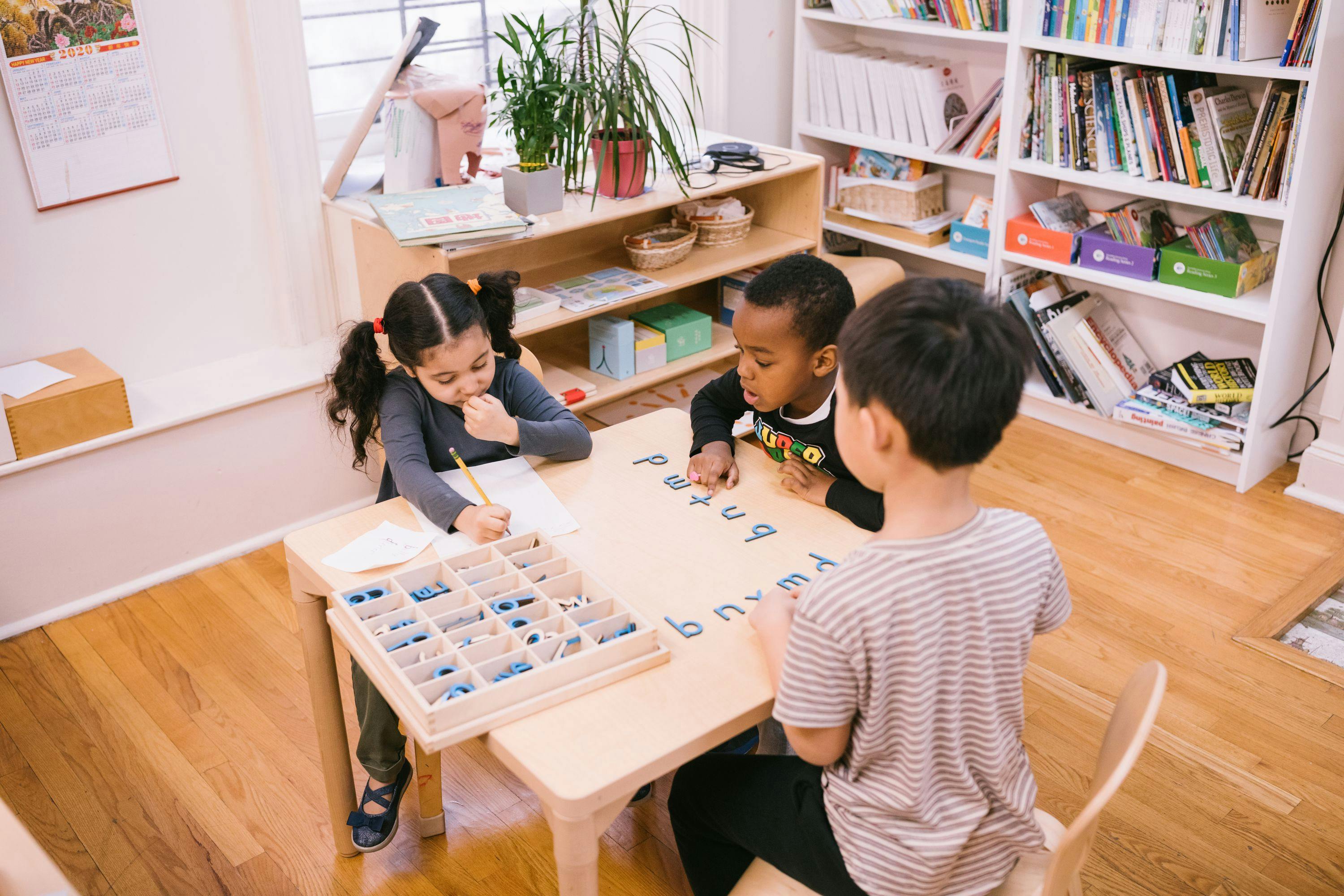 three children in a guidepost montessori kindergarten classroom learning words at a table