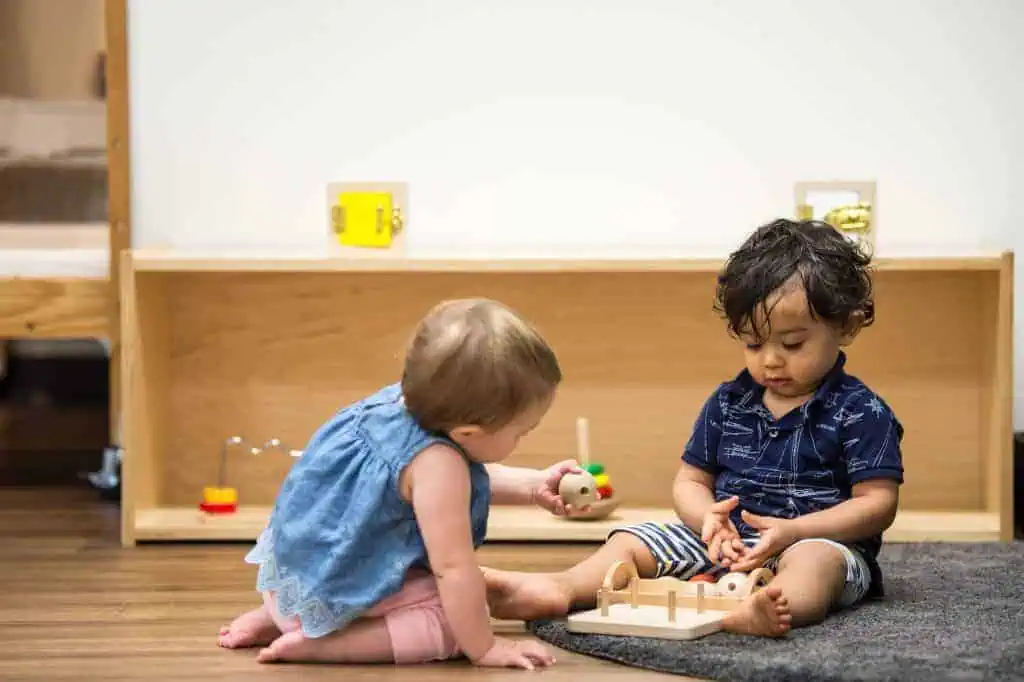 Two infants sharing wooden Montessori toys on the floor of a daycare near me — Guidepost Montessori infant program