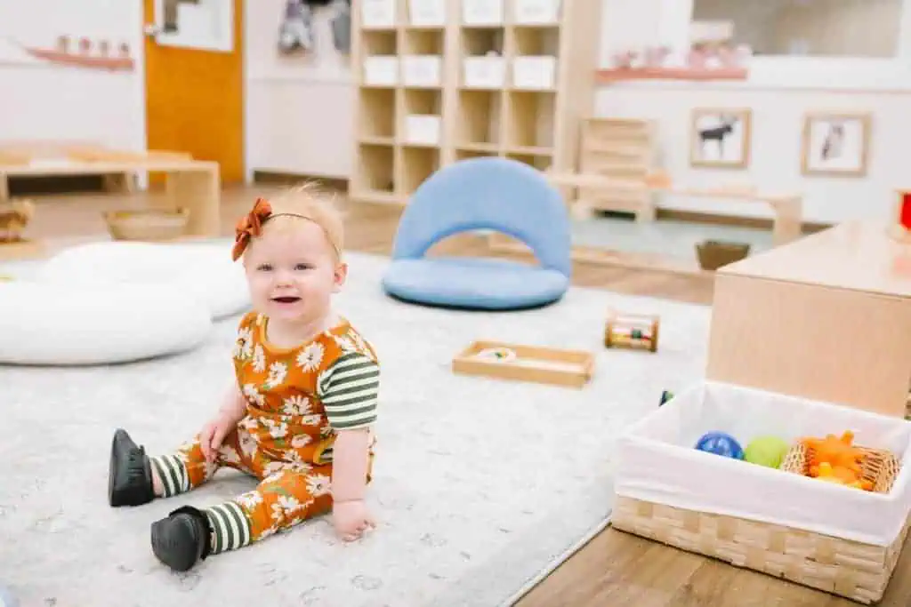 Infant sitting independently on a floor mat in a Montessori classroom, supported by baby essentials that prioritize free movement over containment.