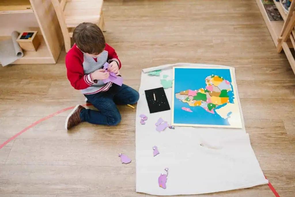 Child working with a Montessori puzzle map on a floor mat at Guidepost Montessori.