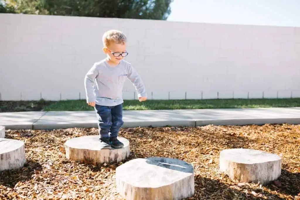 Child balancing on wooden stepping stumps during outdoor play at Guidepost Montessori.