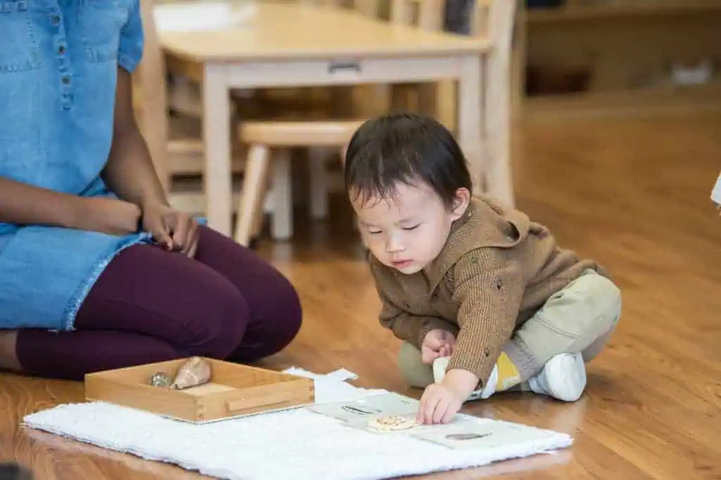 Toddler matching shell objects to cards on a work mat during the Guidepost Montessori experience which is in contrast to overprotected children.