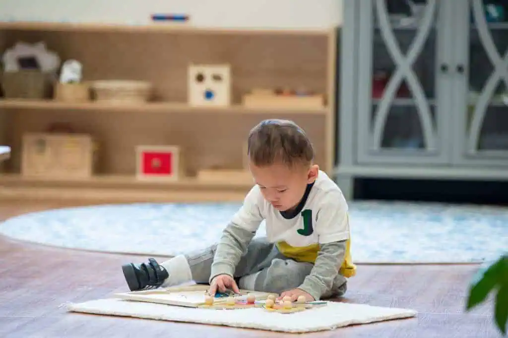 Child using Montessori puzzle material on floor mat during the Guidepost Montessori experience