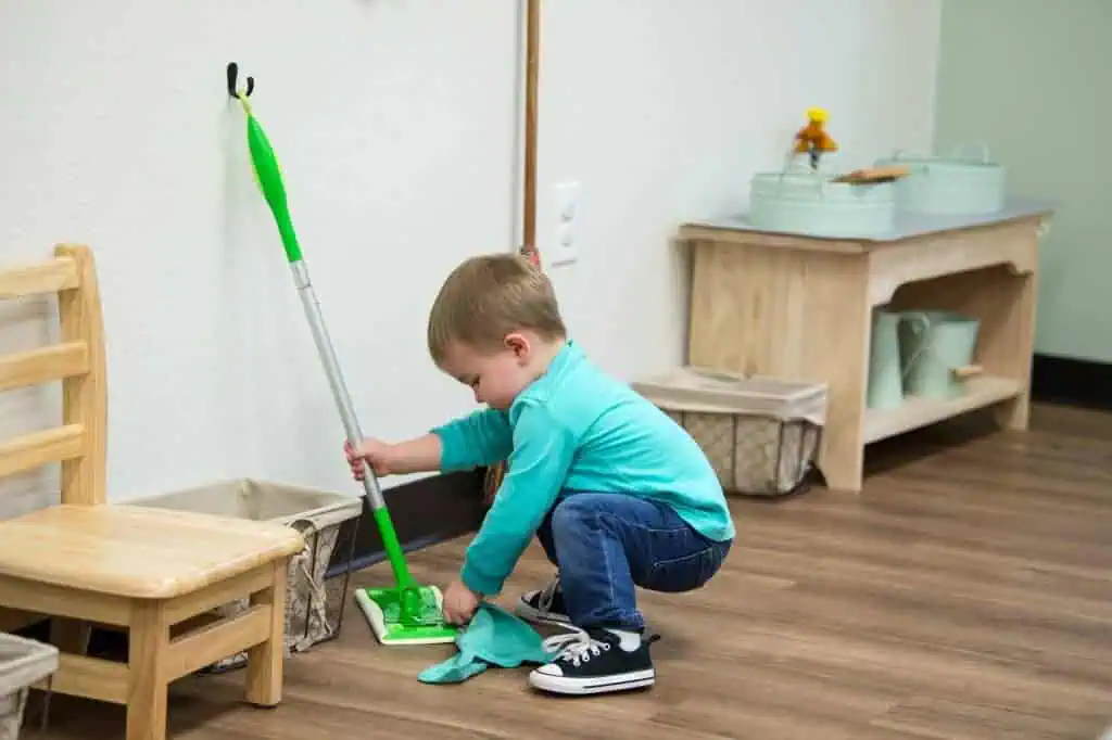 Child cleaning the classroom floor with a mop during practical life work in the Guidepost Montessori experience