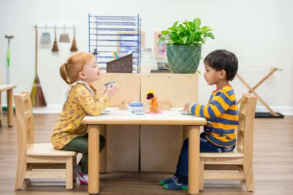 Two young children sharing tea together at a Montessori table during the Guidepost Montessori experience