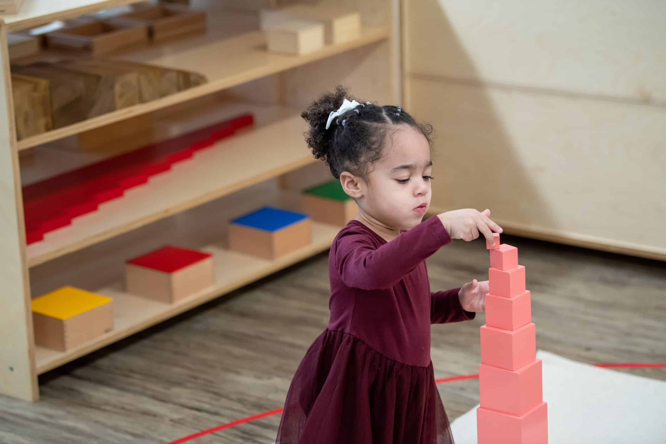 Young child placing the final cube on a completed Montessori pink tower