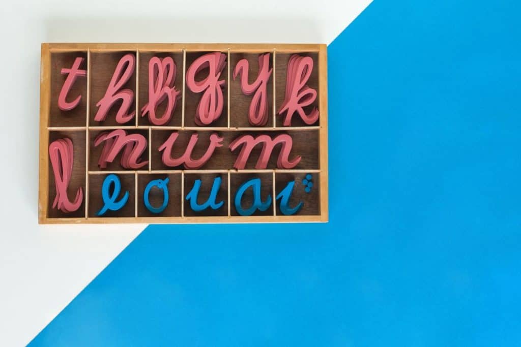Colorful wooden alphabet letters displayed in a wooden box on a blue and white background.